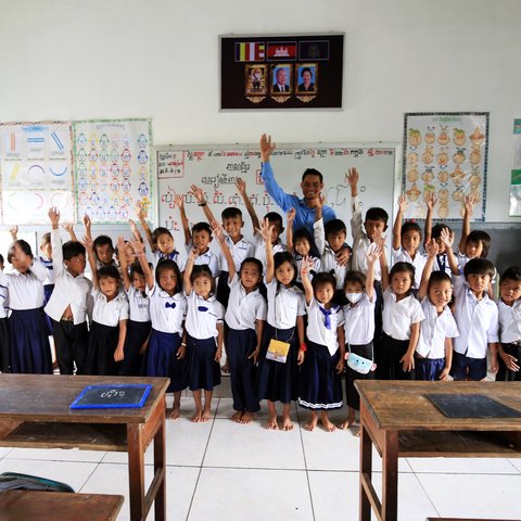 A class of children smile and wave in their classroom in Tonle Sap Lake, Cambodia.
