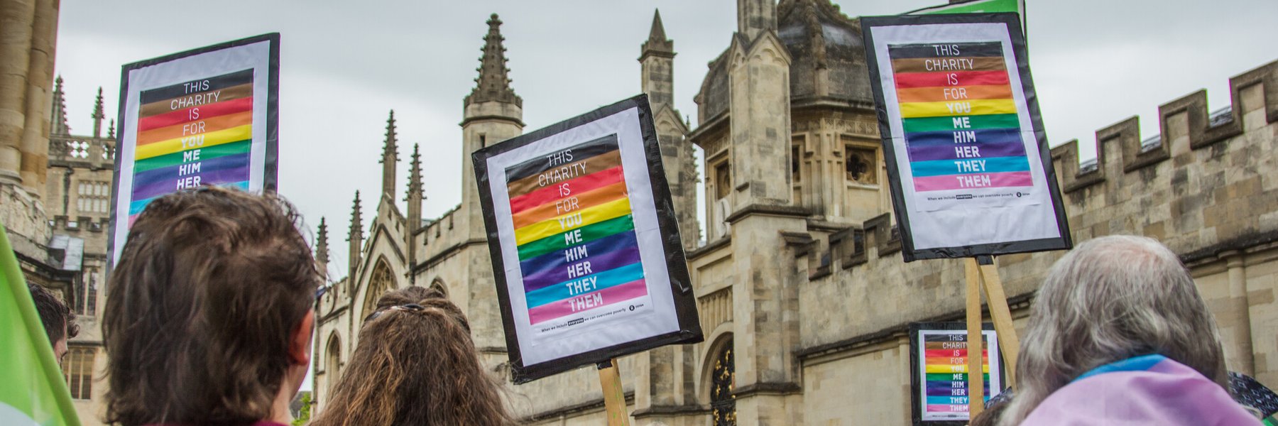 Oxford Pride march featuring three Oxfam LGBTQIA+ placards which read: "this charity is for you me him her they them"