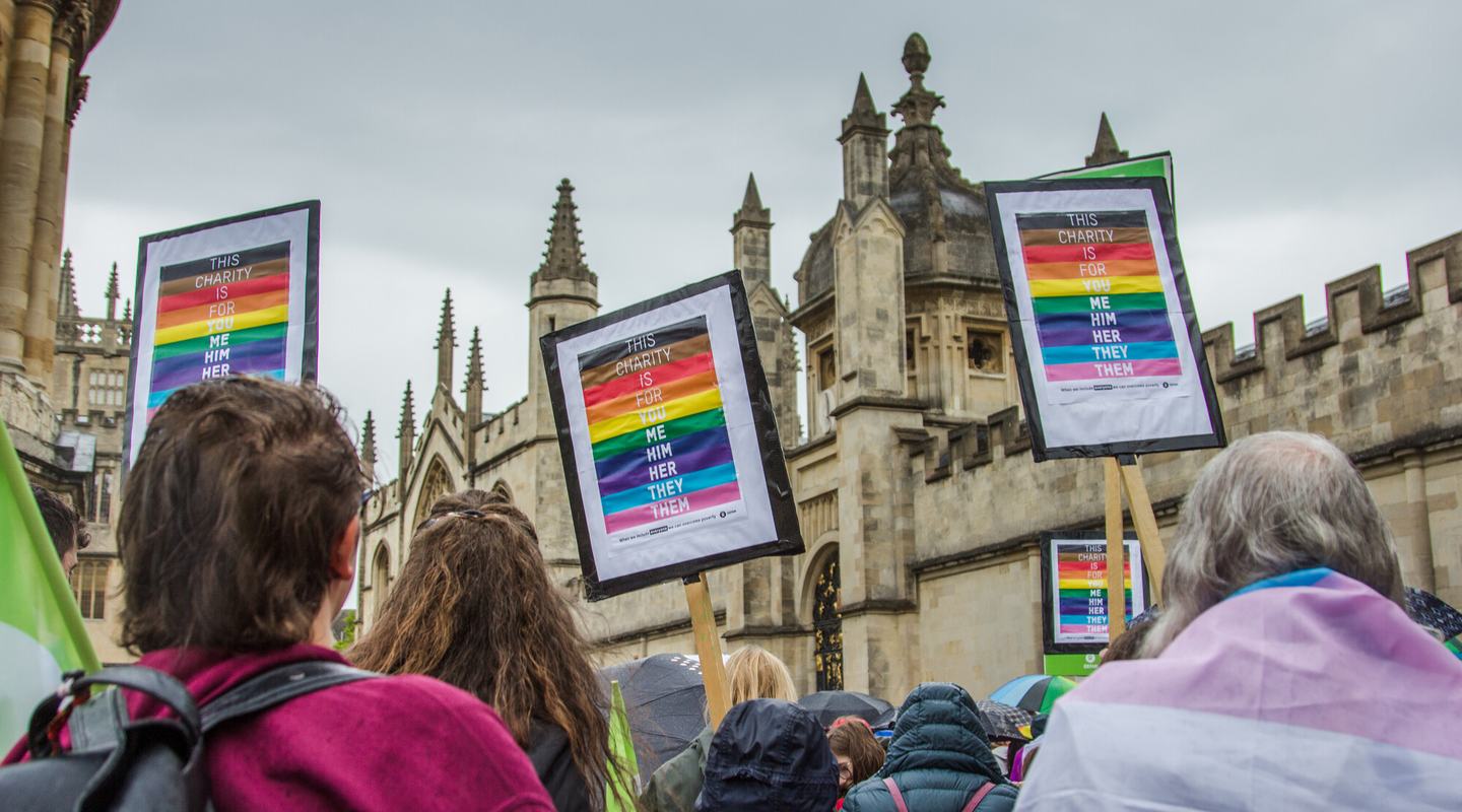 Oxford Pride march featuring three Oxfam LGBTQIA+ placards which read: "this charity is for you me him her they them"