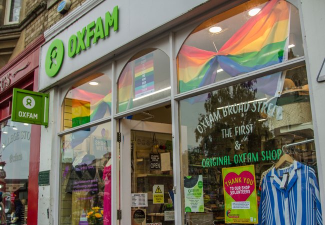 Pride flags and volunteer posters in window of Oxfam shop in Broad Street, Oxford,UK.