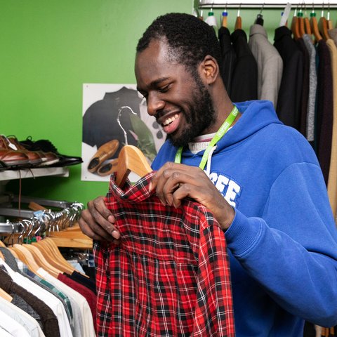 Andrew holds a red checked shirt by a clothes rail in an Oxfam shop