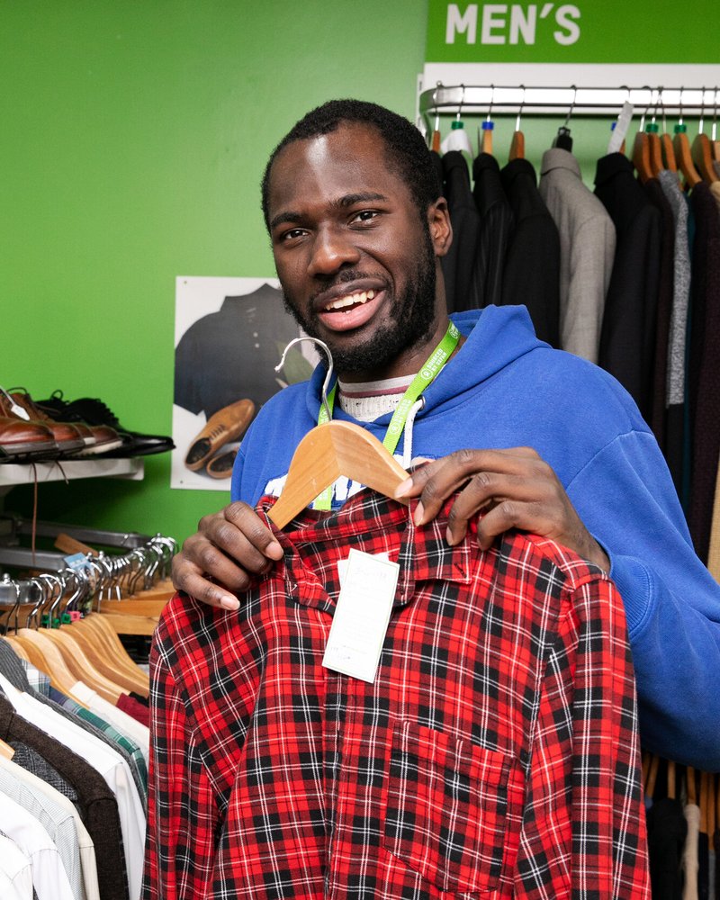 Oxfam shop volunteer Andrew holding up a donated red shirt on a clothes hanger.