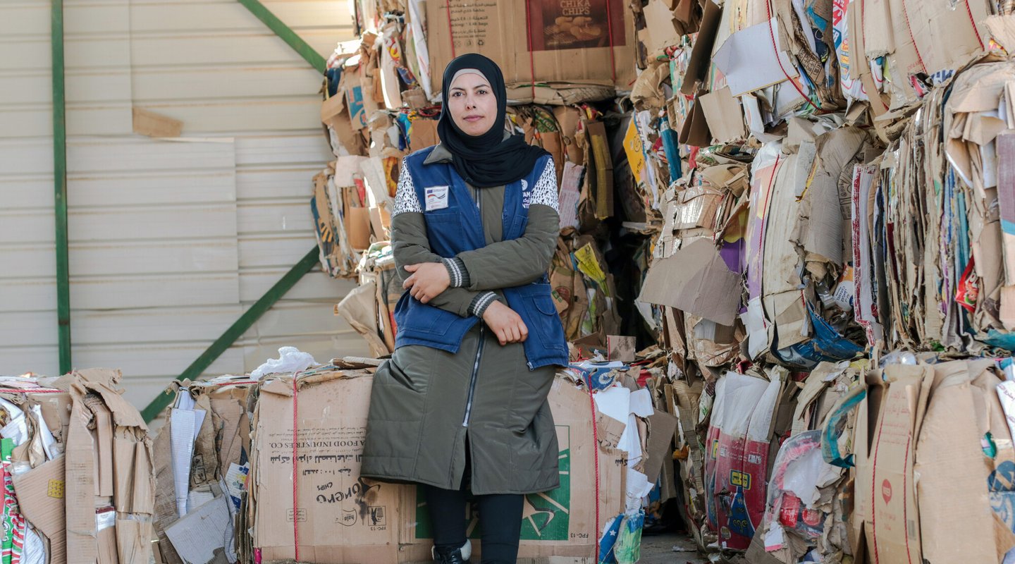 Hamda wears a black hijab and sits surrounded by cardboard packed up for recycling.