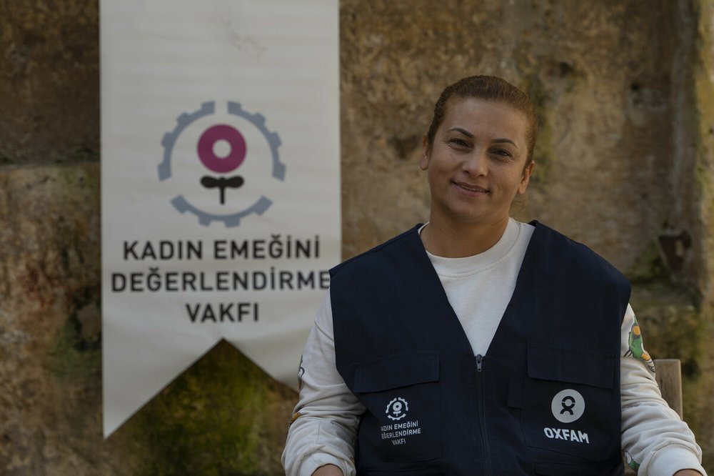 Türkan is standing in front of a stone wall where the KEDV banner is hanging next to her.