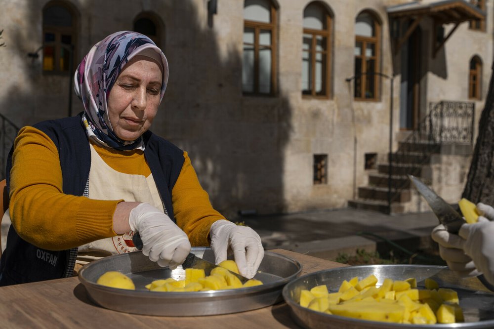 A woman cuts fruit on a metal plate. She is wearing gloves.