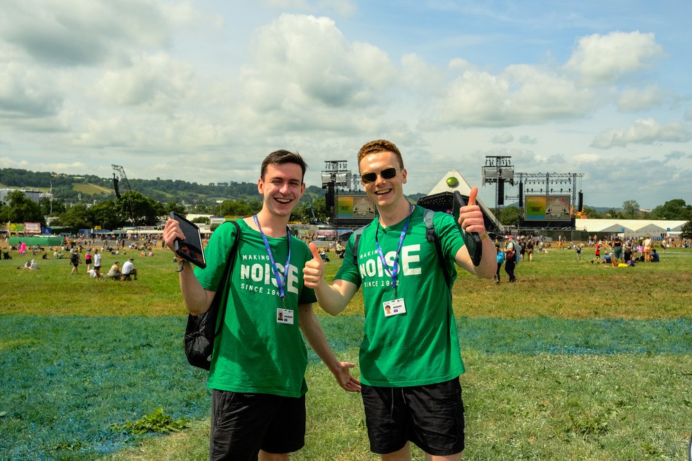 Two Oxfam campaigners standing together in green Oxfam t-shirts at Glastonbury 2023.