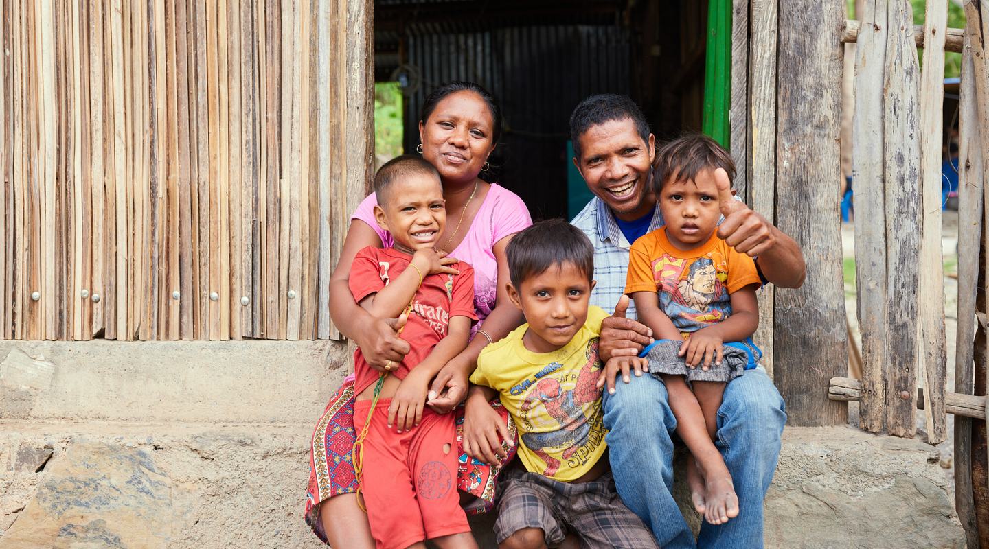 A woman and her husband sit with their children on the step outside their house in Timor-Leste.