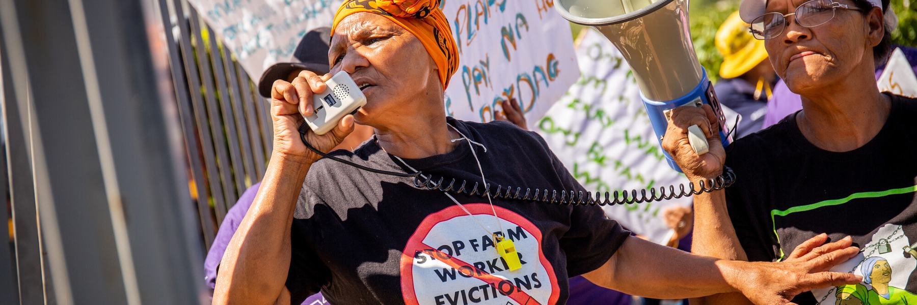 A woman wearing a t-shirt reading 'Stop farm worker evictions' speaks into a megaphone as she leads a protest in De Doorns, South Africa.
