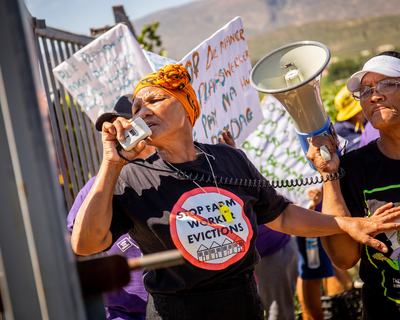 A woman wearing a t-shirt reading 'Stop farm worker evictions' speaks into a megaphone as she leads a protest in De Doorns, South Africa.
