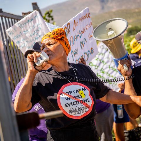 A woman wearing a t-shirt reading 'Stop farm worker evictions' speaks into a megaphone as she leads a protest in De Doorns, South Africa.