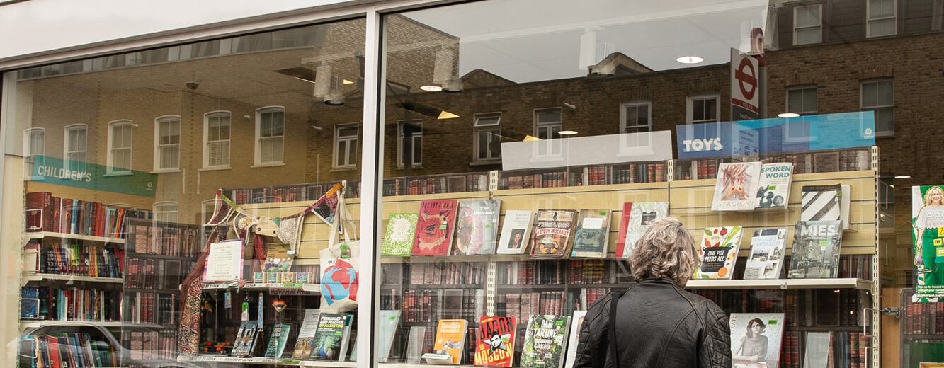 An exterior shot of a man standing looking into the window of an Oxfam shop , featuring a large selection of donated books in the window display.