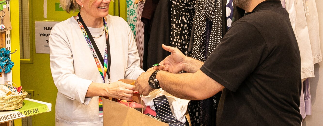 A person making a donation of clothing to a smiling Oxfam Shop team member, inside an Oxfam Shop