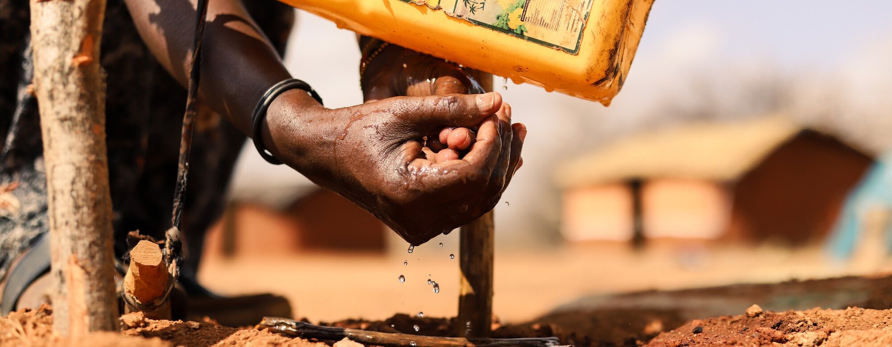 A close up of hands with water on them from a yellow jerry can above them.