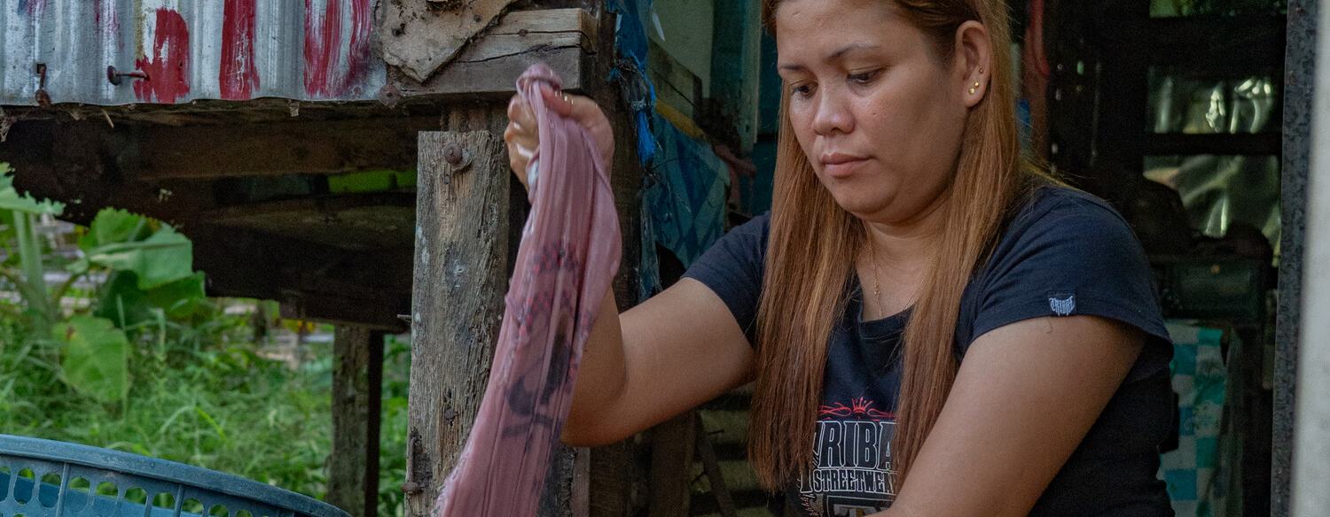 A young woman is crouched outside her home washing some clothes in a large tub.