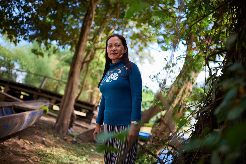 A woman standing on a river bank surrounded by boats and trees.