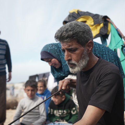 A man looks serious holding a poker for a bread oven with his family in the background.