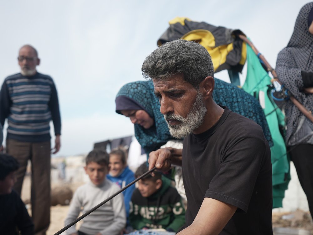 A man looks serious holding a poker for a bread oven with his family in the background.