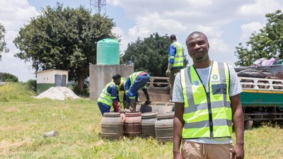 A Zambian man in a hi vis Oxfam jacket with men at work in the background.