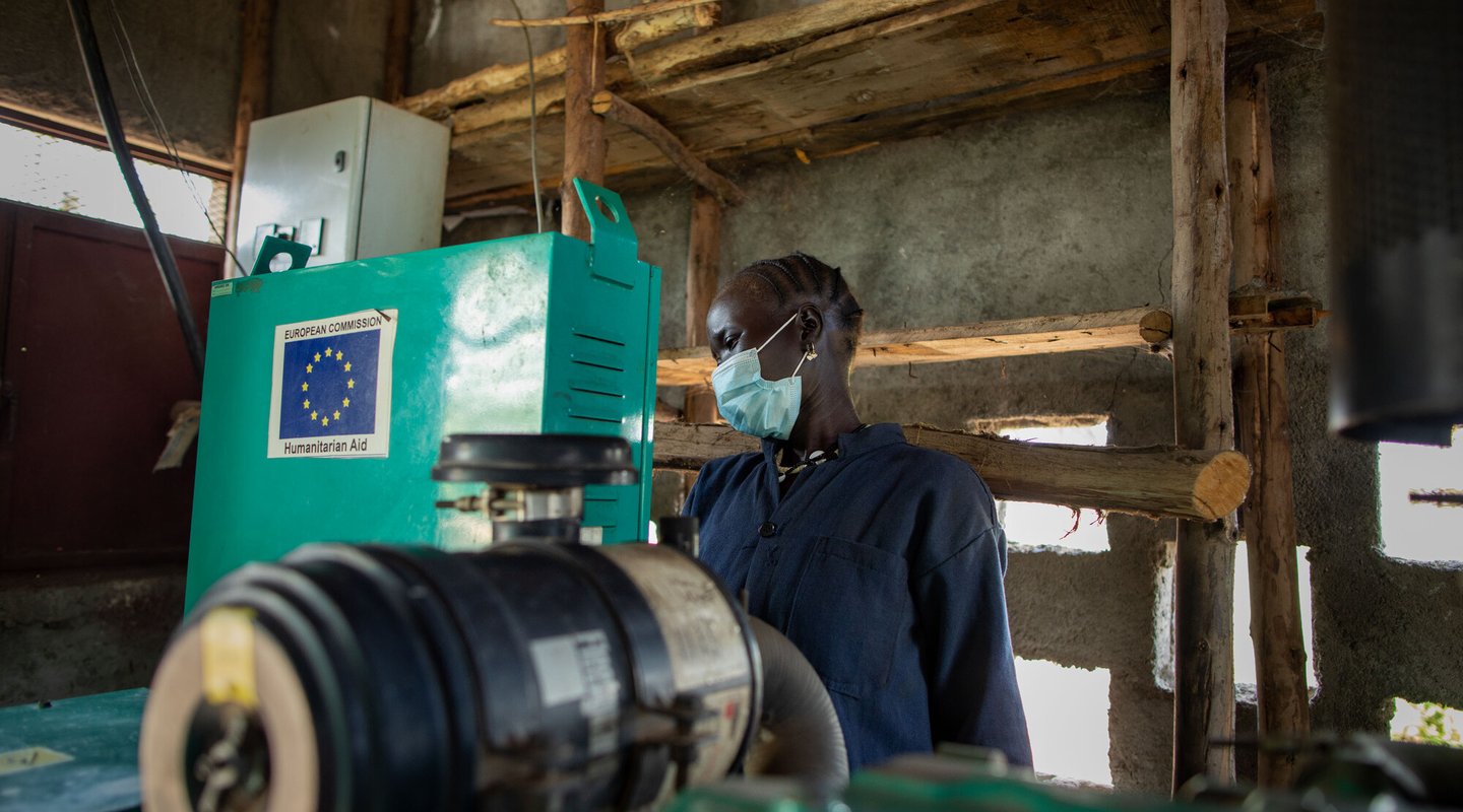 Ethiopian woman Nyathak stands behind green machinery wearing a facemask and blue boilersuit