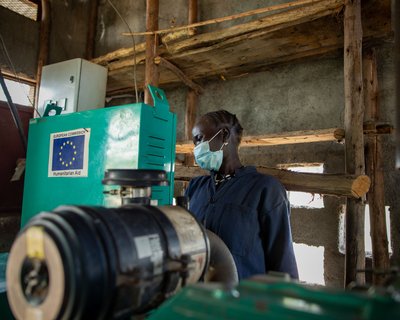 Ethiopian woman Nyathak stands behind green machinery wearing a facemask and blue boilersuit