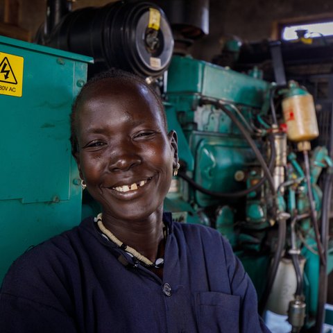 Ethiopian woman Nyathak stands smiling in a blue boilersuit next to green machinery