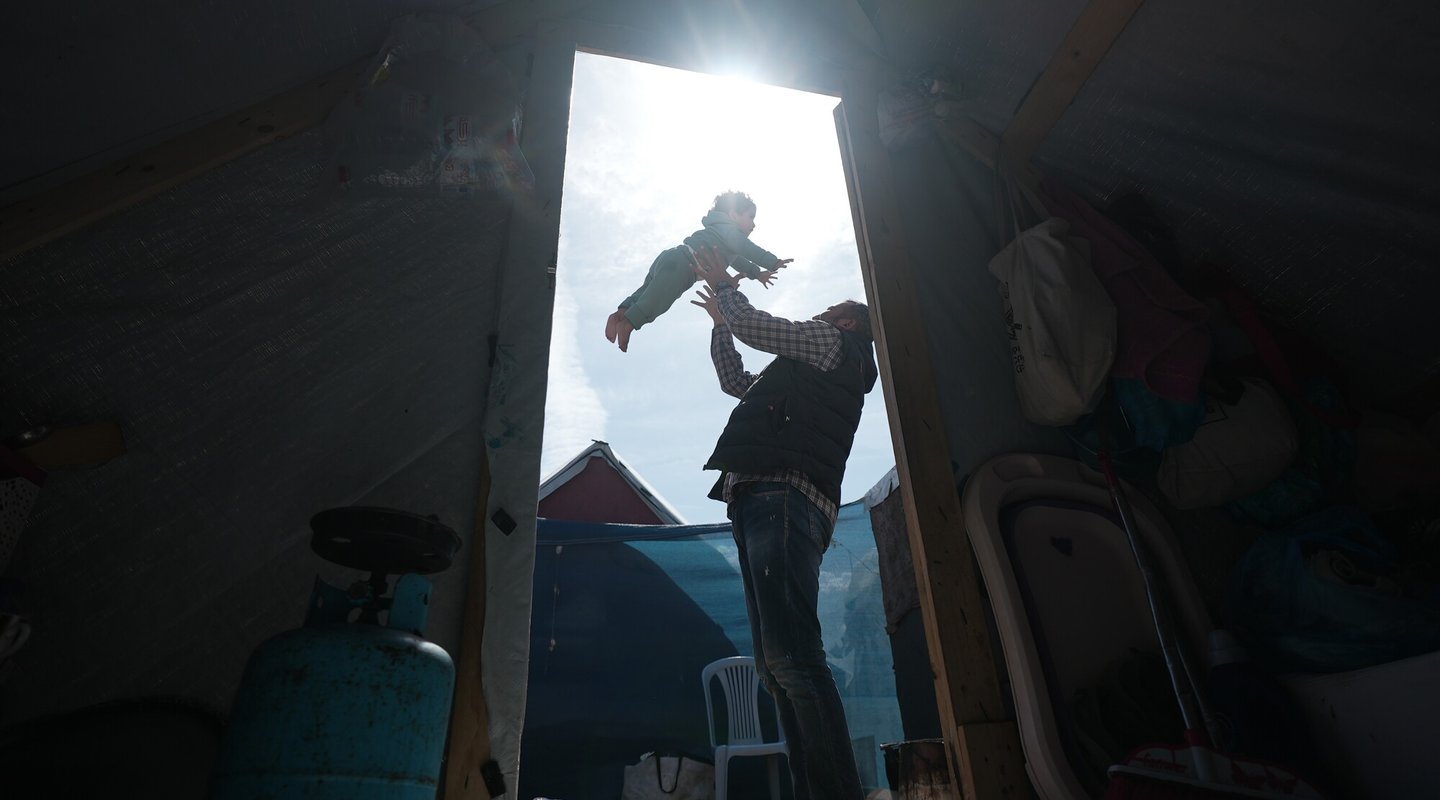 A father playfully throws his 3-year-old daughter in the air, outside the entrance to their tent in Gaza.