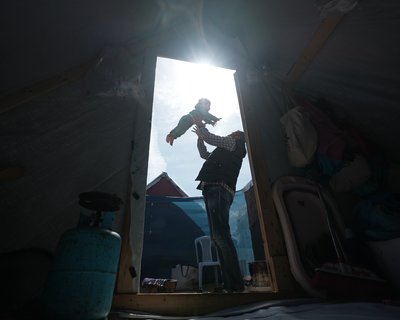 A father playfully throws his 3-year-old daughter in the air, outside the entrance to their tent in Gaza.