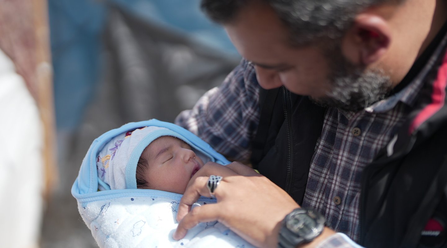 A father looks over his little baby which is wrapped in a baby blanket.