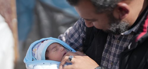 A father looks over his little baby which is wrapped in a baby blanket.