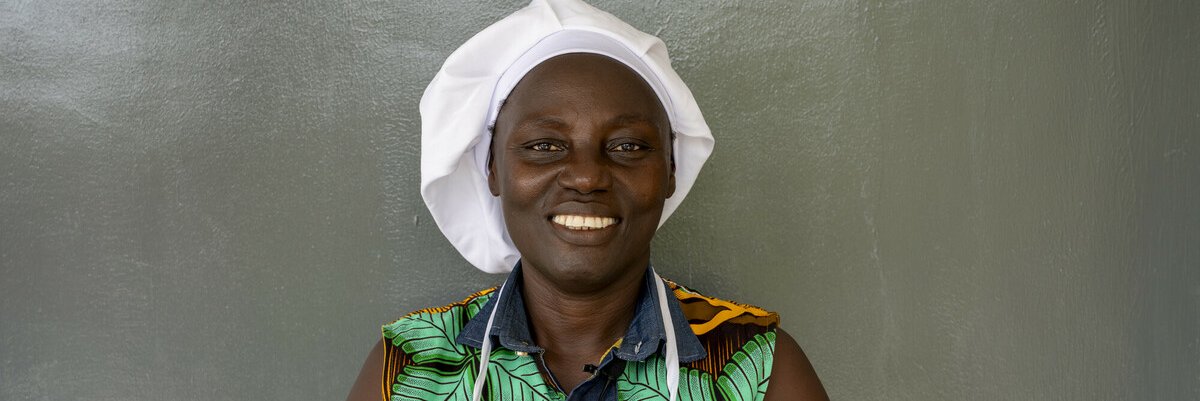 Smiling black woman wearing chef's hat looks directly at camera