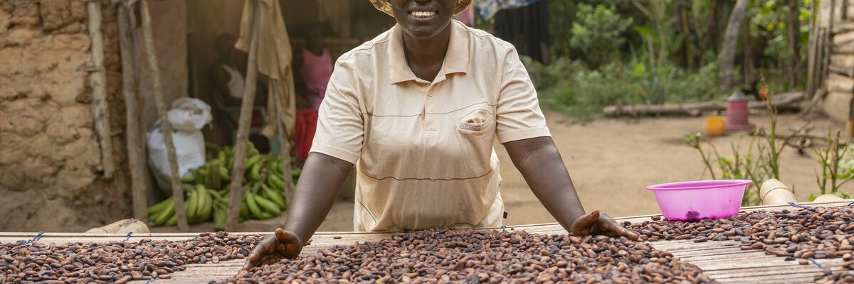 Smiling woman in centre of photo, there are lots of coca beans in front of her on a table