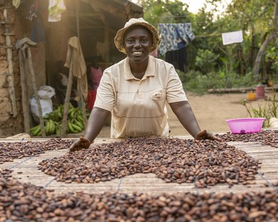 Smiling woman in centre of photo, there are lots of coca beans in front of her on a table
