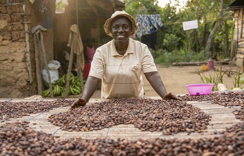 Smiling woman in centre of photo, there are lots of coca beans in front of her on a table