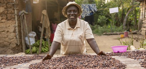 Leticia smiles as she stands behind a table of drying beans on at her farm in Ghana.