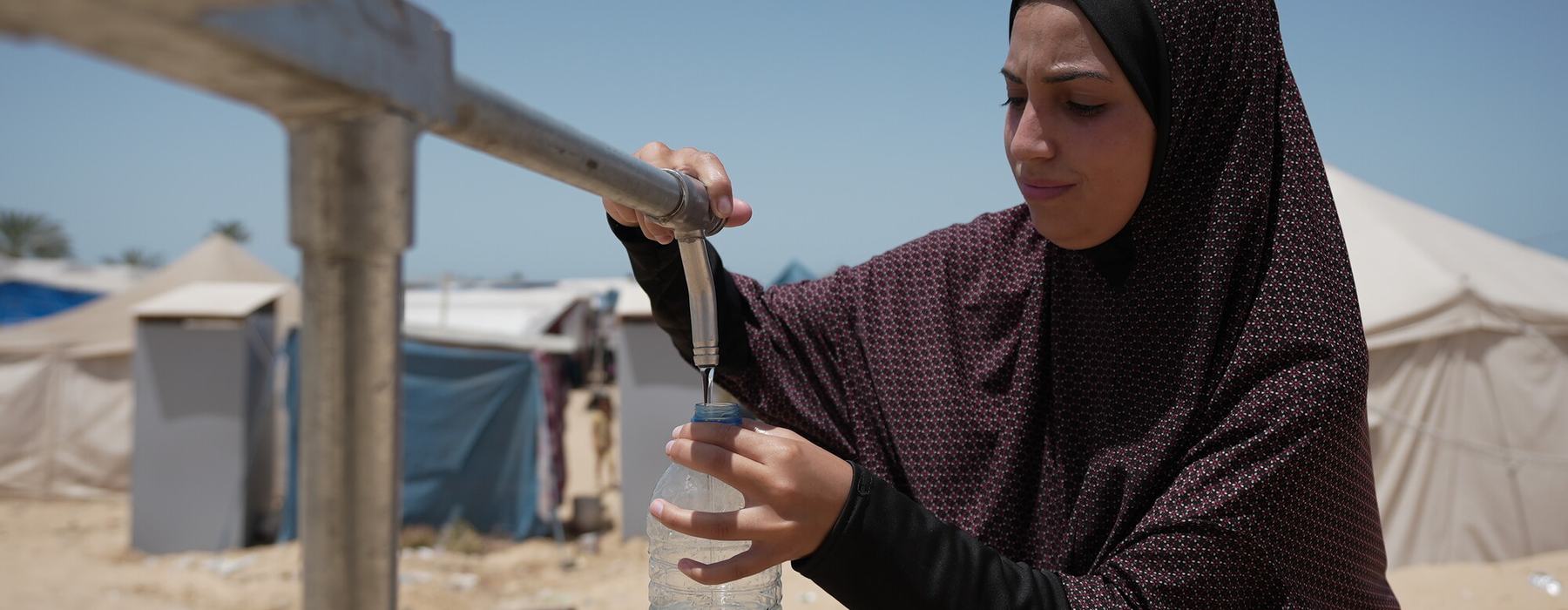 Duaa Abu Sabha filling water bottles from Oxfam's water tank.