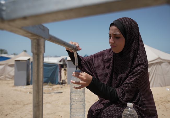 Duaa Abu Sabha filling water bottles from Oxfam's water tank.
