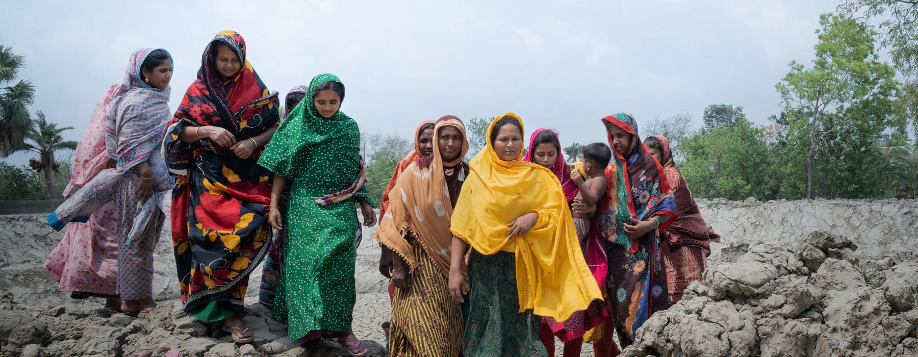 A group of women from a in Satkhira, Bangladesh walking along a rocky terrain impacted by climate change and increasing levels of salinity in the water.