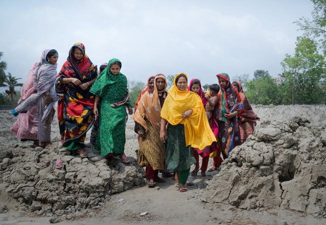 A group of women from a in Satkhira, Bangladesh walking along a rocky terrain impacted by climate change and increasing levels of salinity in the water.