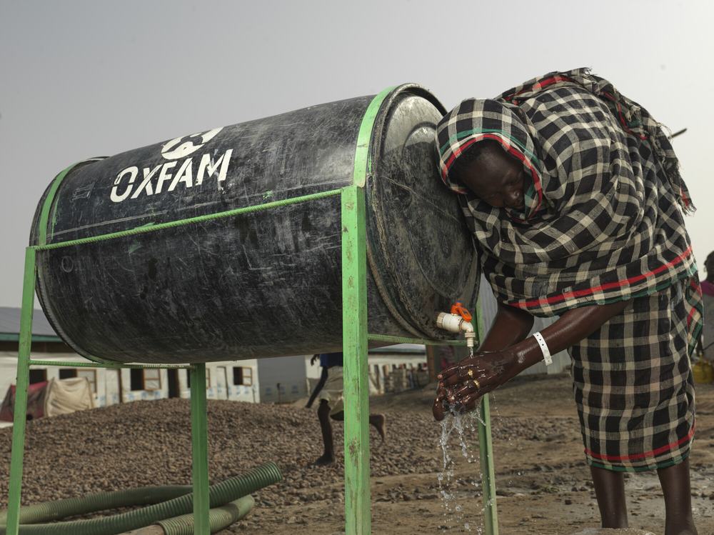 a woman stood next to a water tank, washing her hands under the tap.