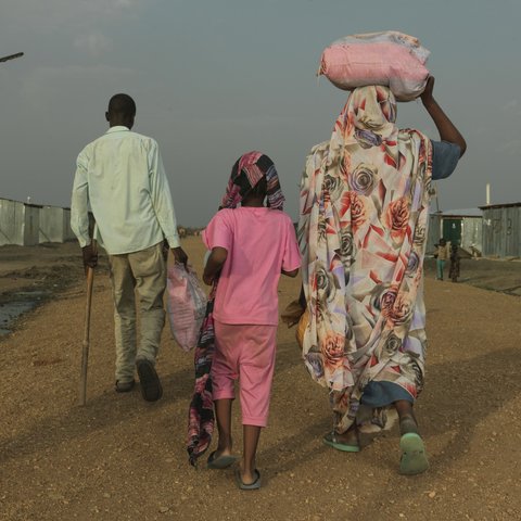 A family of three walking away from the camera in a transit centre in South Sudan