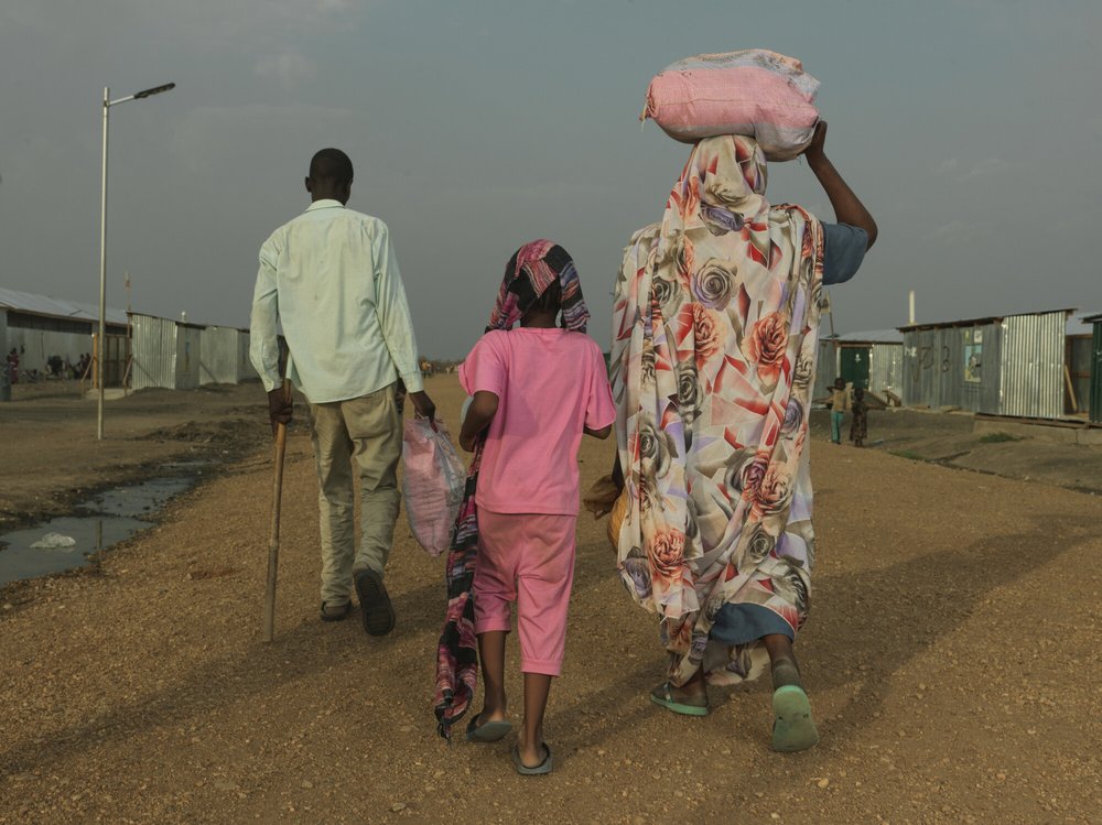 A family of three walking away from the camera in a transit centre in South Sudan
