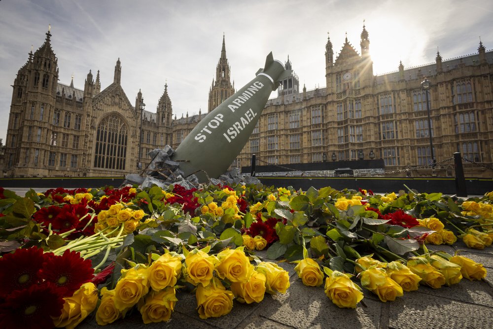 A replica bomb that says 'stop arming Israel' on it surrounded by red and yellow flowers outside UK parliament.