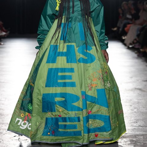 Model walking a glamourous catwalk, wearing sunglasses and a huge dress with letters on it