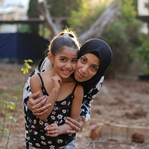 Siham, a displaced woman in Tripoli, North Lebanon, smiles as she hugs her 7-year-old daughter.