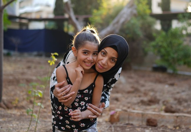 Siham, a displaced woman in Tripoli, North Lebanon, smiles as she hugs her 7-year-old daughter.