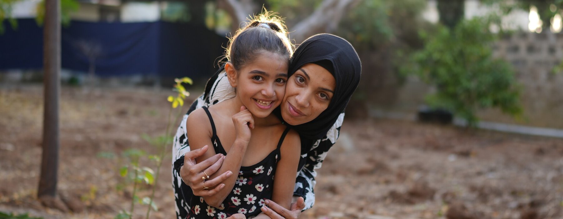 Siham, a displaced woman in Tripoli, North Lebanon, smiles as she hugs her 7-year-old daughter.