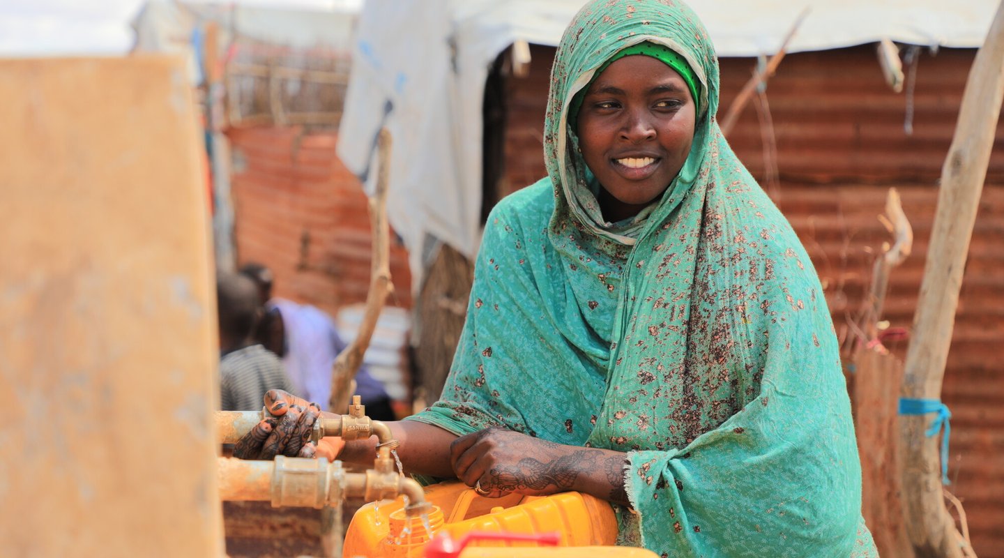 Aqiqah, a mother of three collects water from an Oxfam-constructed water tank