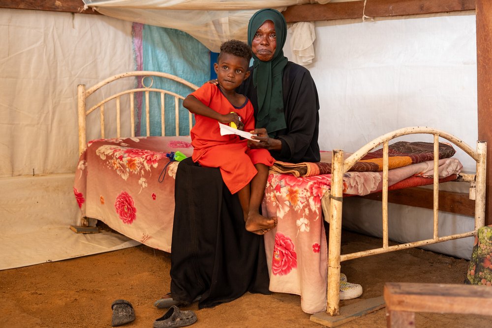 35-year-old Nadia Zahad, a refugee from the Sudan war, sits on the edge of a bed inside a tent in South Sudan. Her son Ismail is on her lap.