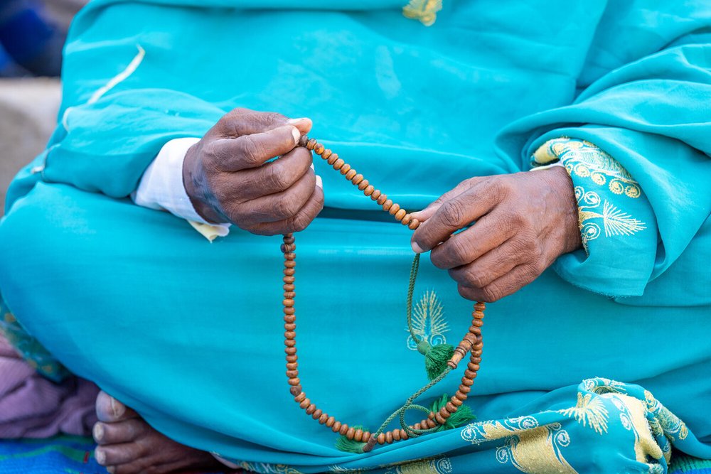 A close up of the hands of a woman sitting cross-legged. She is holding a string of prayer beads/