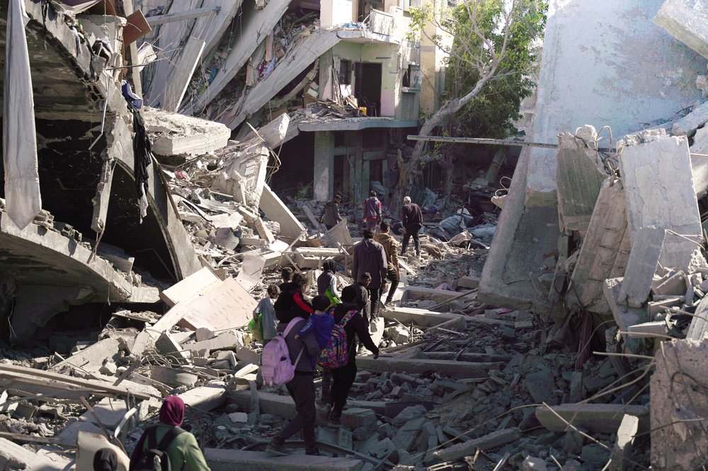 Children and their families walking in single file through the rubble of destroed buildings in Northern Gaza